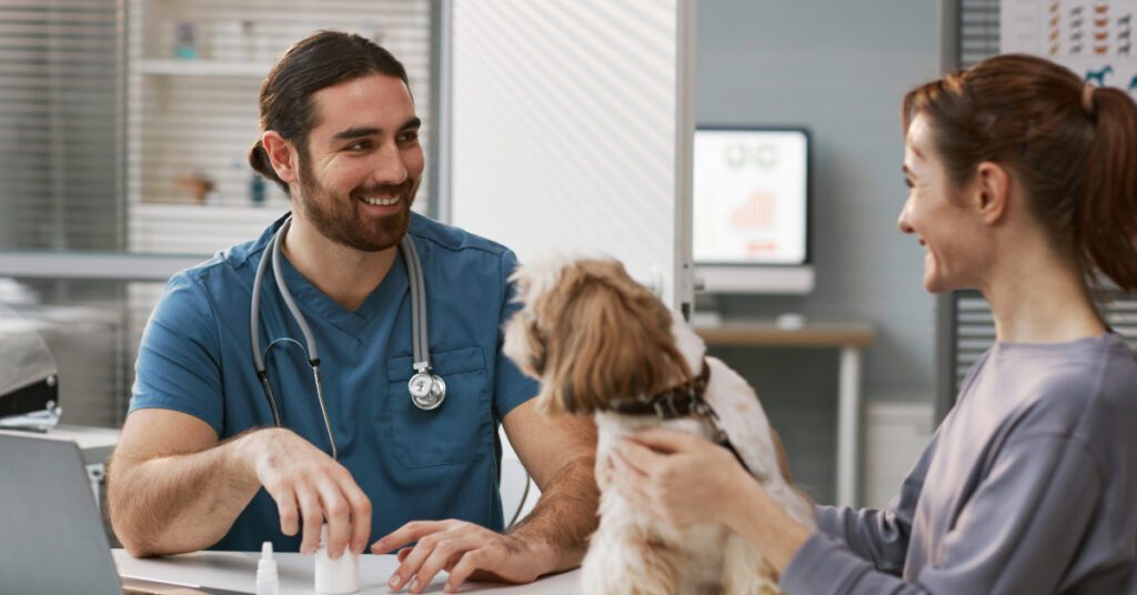 female dog owner petting dog while talking with male vet at clinic